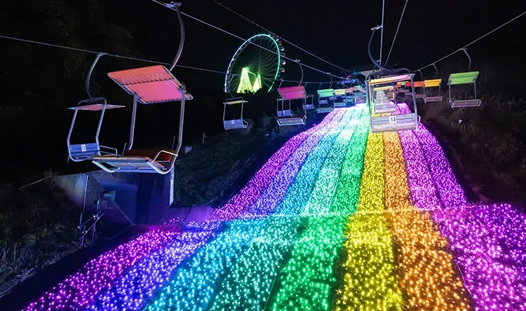 A chairlift above a rainbow slope of lights at Sagamiko Illumillion